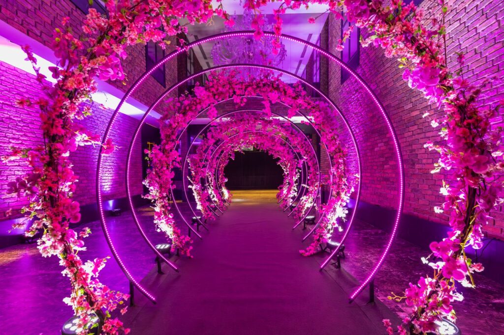Floral-decorated corridor with vivid purple lights and elegant arches, perfect for celebrations.